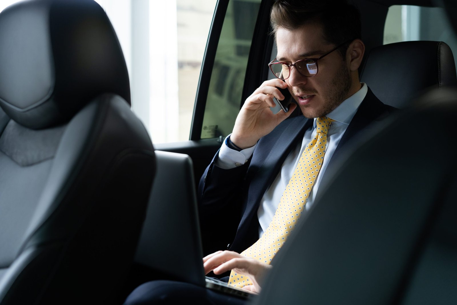 young businessman sitting back seat car while his chauffeur is driving automobile scaled